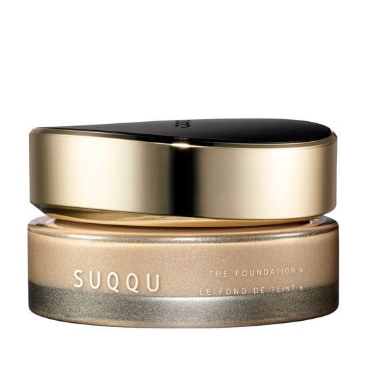 SUQQU The Foundation e 020 luxury cream base makeup jar on plain white background with gold and black lid and frosted glass base. Light beige cream foundation shade.
