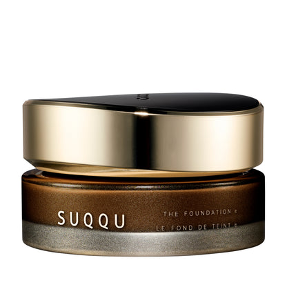 SUQQU The Foundation e 180 luxury cream base makeup jar on plain white background with gold and black lid and frosted glass base. Dark brown cream foundation shade.