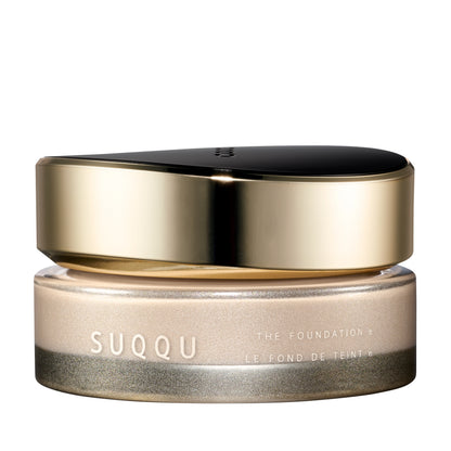 SUQQU The Foundation e 200 luxury cream base makeup jar on plain white background with gold and black lid and frosted glass base. Very pale light beige cream foundation shade.