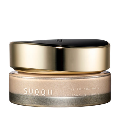 SUQQU The Foundation e 210 luxury cream base makeup jar on plain white background with gold and black lid and frosted glass base. Pale light beige cream foundation shade.