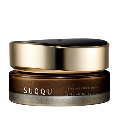 SUQQU The Foundation e 290 luxury cream base makeup jar on plain white background with gold and black lid and frosted glass base. Dark brown cream foundation shade with rose undertone.