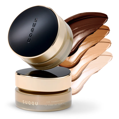 SUQQU The Foundation e jar shown with a black lid and gold rim, layered over stacked foundation swatches in dark brown, tan, and light beige on a white background.
