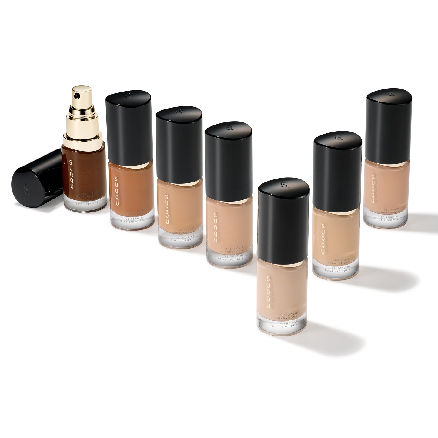 Seven SUQQU The Liquid Foundation e products standing on a table with a cap off to show pump nozzle