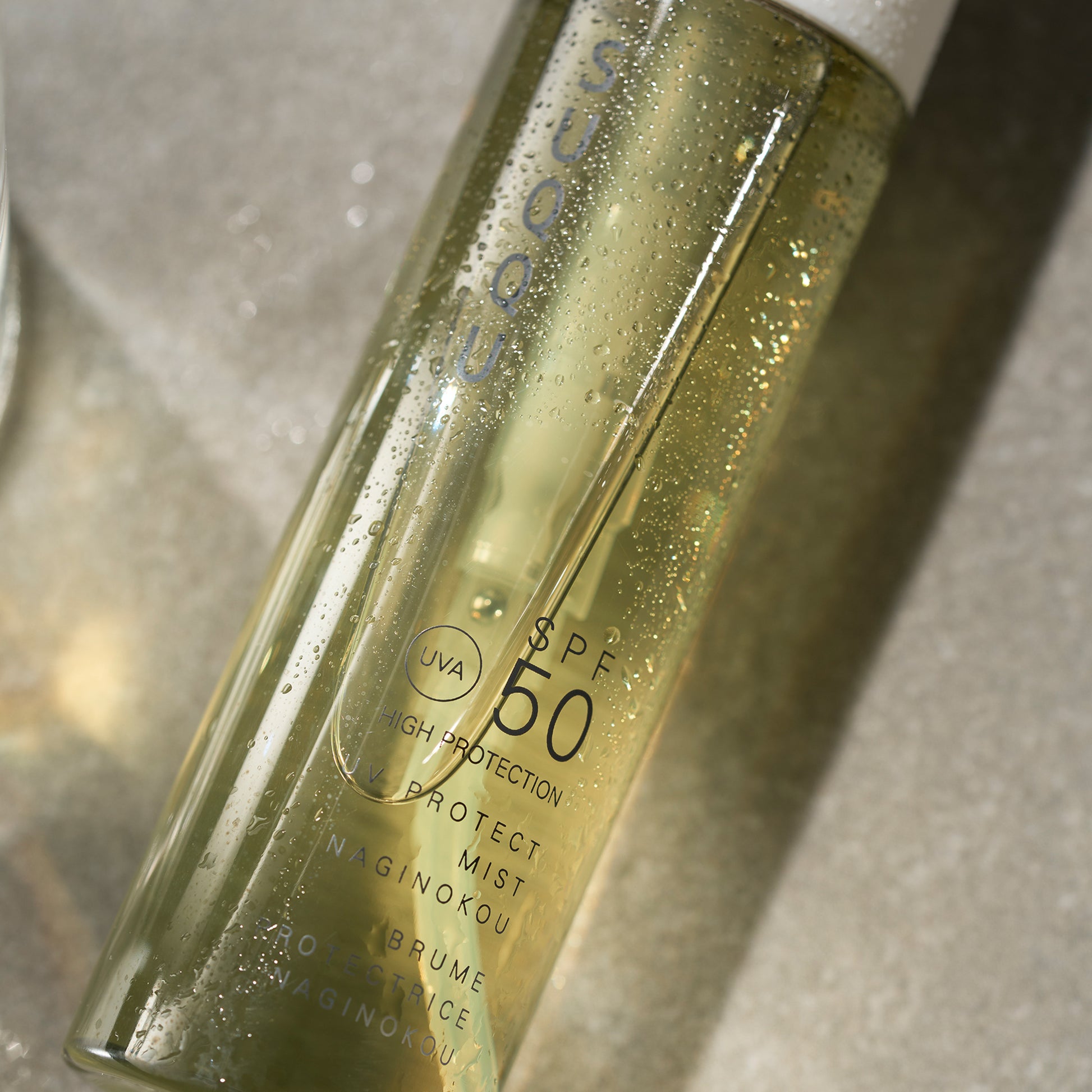 SUQQU UV Protect Mist Naginokou SPF 50 reliable Japanese premium sun care pump bottle covered with glistening water droplets.