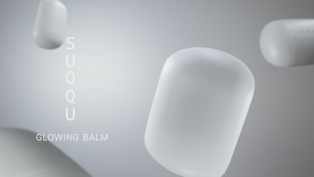 Multiple SUQQU Glowing Balm products floating and rotating. Product is shown on a table with other personal effects, then being open and applied to the back of the hand and face with a close up a model.