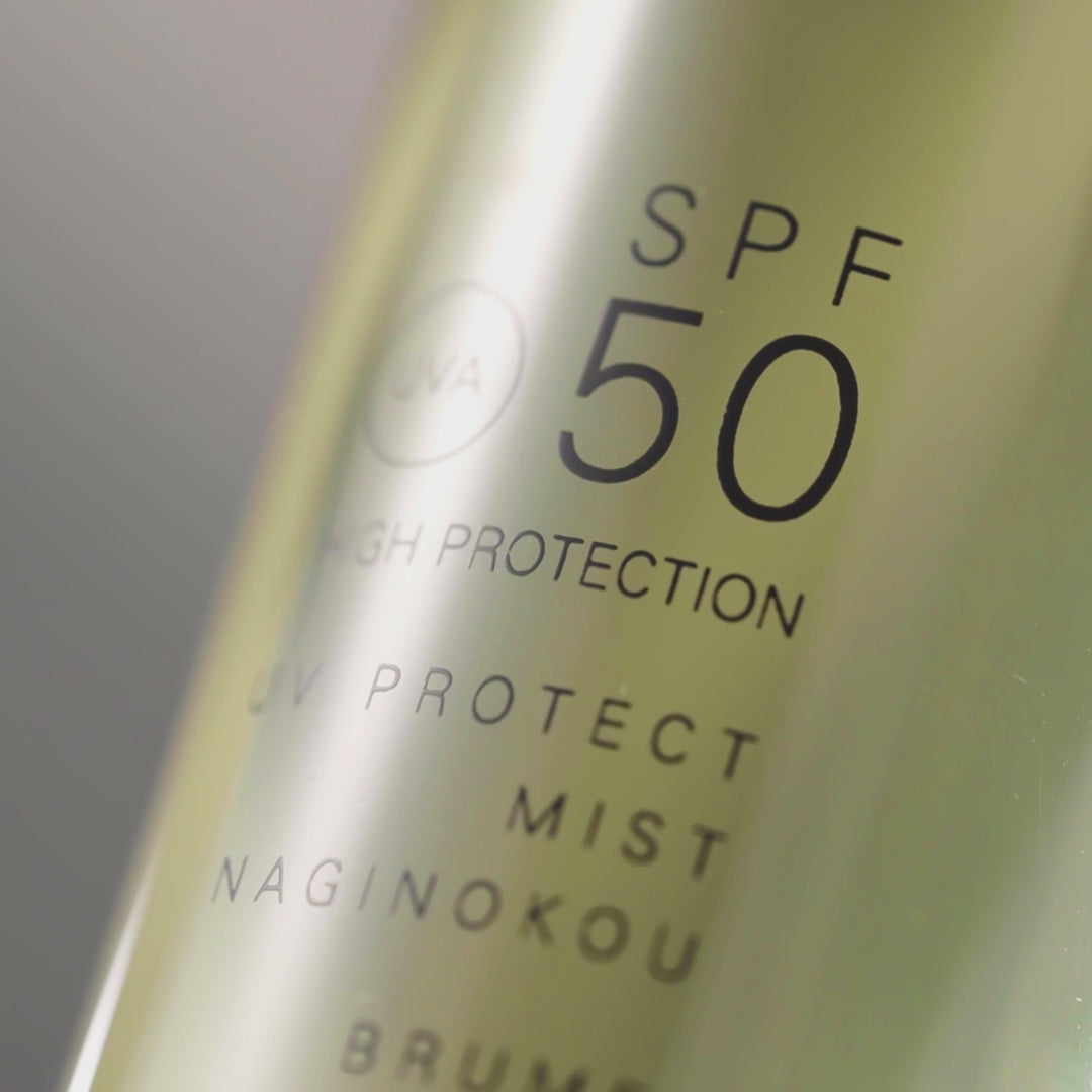 SUQQU UV Protect Mist Naginokou SPF 50 sun care pump bottle sprayed into the air. Icons with text read: SPF50 Effective UVA/UVB Protection. Body, Face & Hair, non-greasy or sticky finish. Water-resistant reliable suncare. Beautiful Naginokou botanical scent.