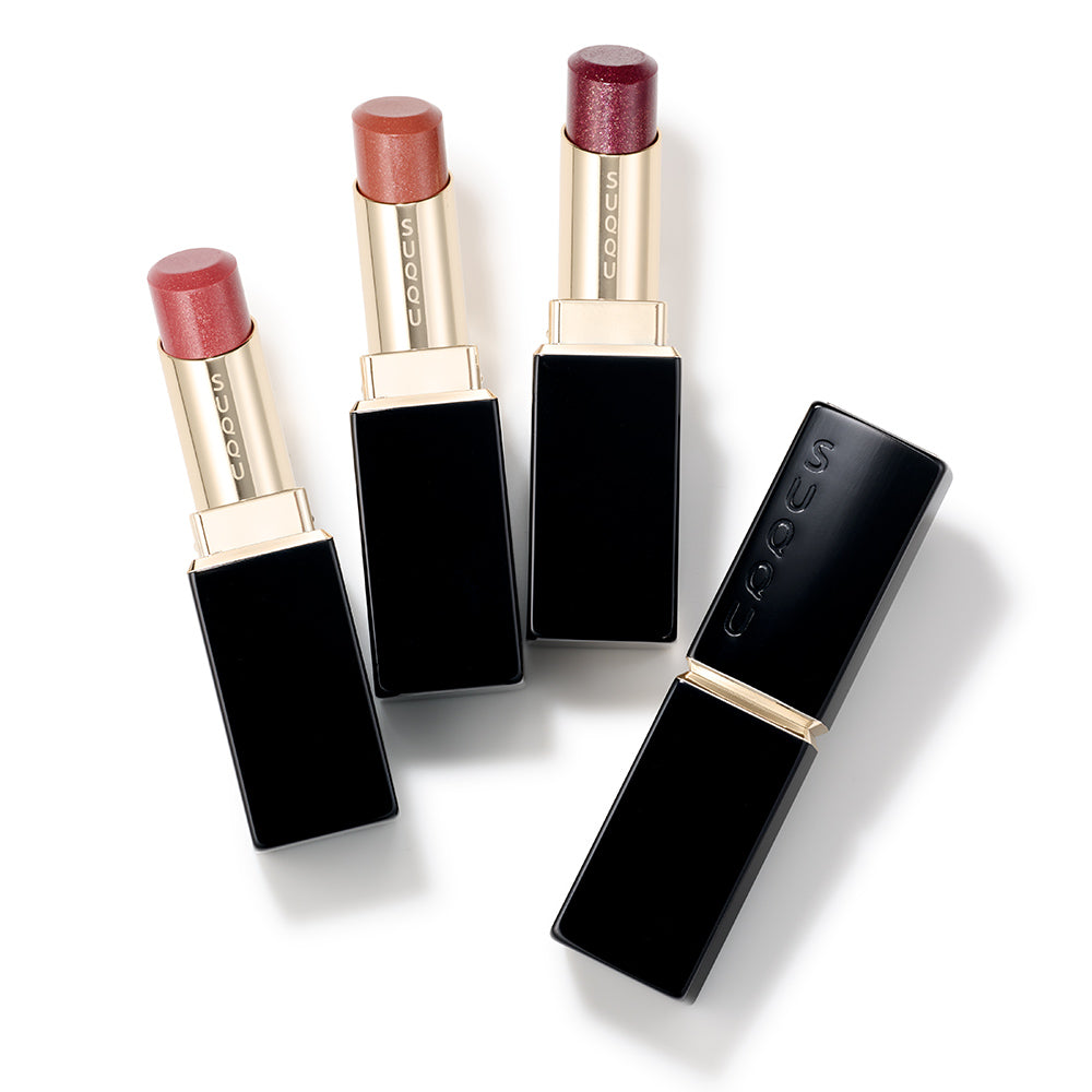 Three SUQQU Moisture Glaze Lipsticks in 114, 115 and 116 shimmering shades with closed case on white background.